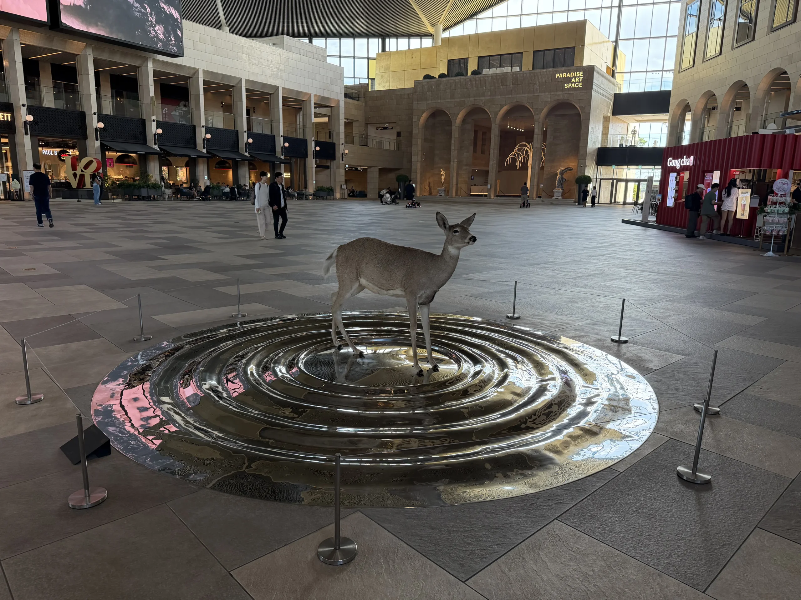 パラダイスシティPLAZAの広いアトリウム中央に展示された鹿のアート作品と周辺のショップ