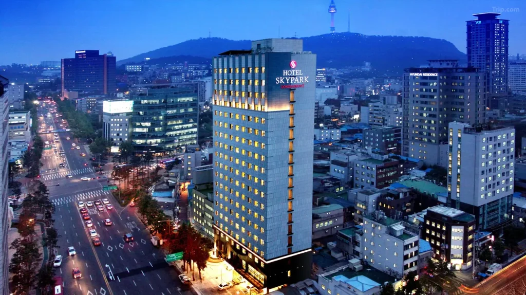 韓国ソウル・東大門のホテルスカイパーク東大門Iの夕暮れの外観。ライトアップされたホテルと背景のNソウルタワー、周辺の街並みを望む夜景。