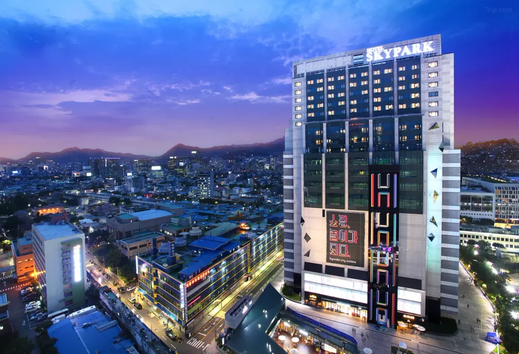 韓国ソウルのホテルスカイパークキングスタウン東大門の夕暮れの外観。ライトアップされたホテルと東大門の街並みを望む夜景。