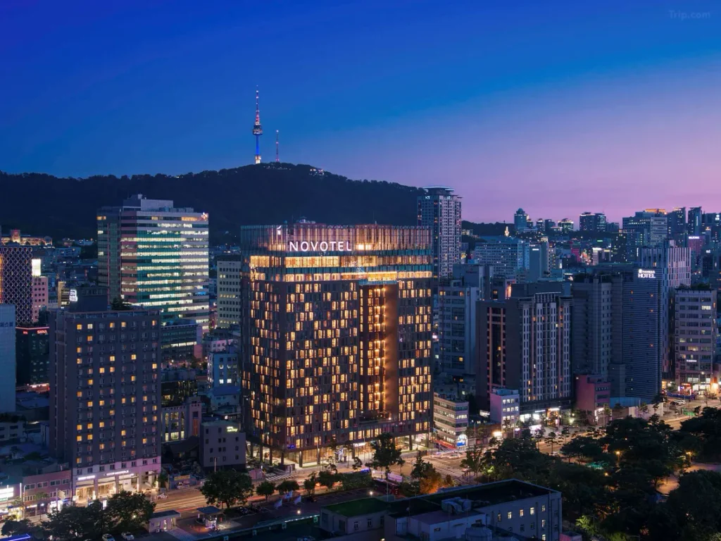 韓国ソウルのノボテルアンバサダーソウル東大門の夕暮れの外観。ライトアップされたホテルとNソウルタワーを望む東大門エリアの夜景。