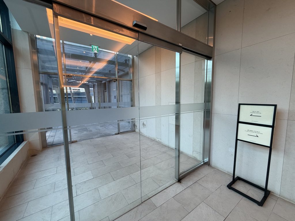 スカイブリッジのガラス製自動ドアと、右側に設置されたフィットネスセンターなどの方向案内板