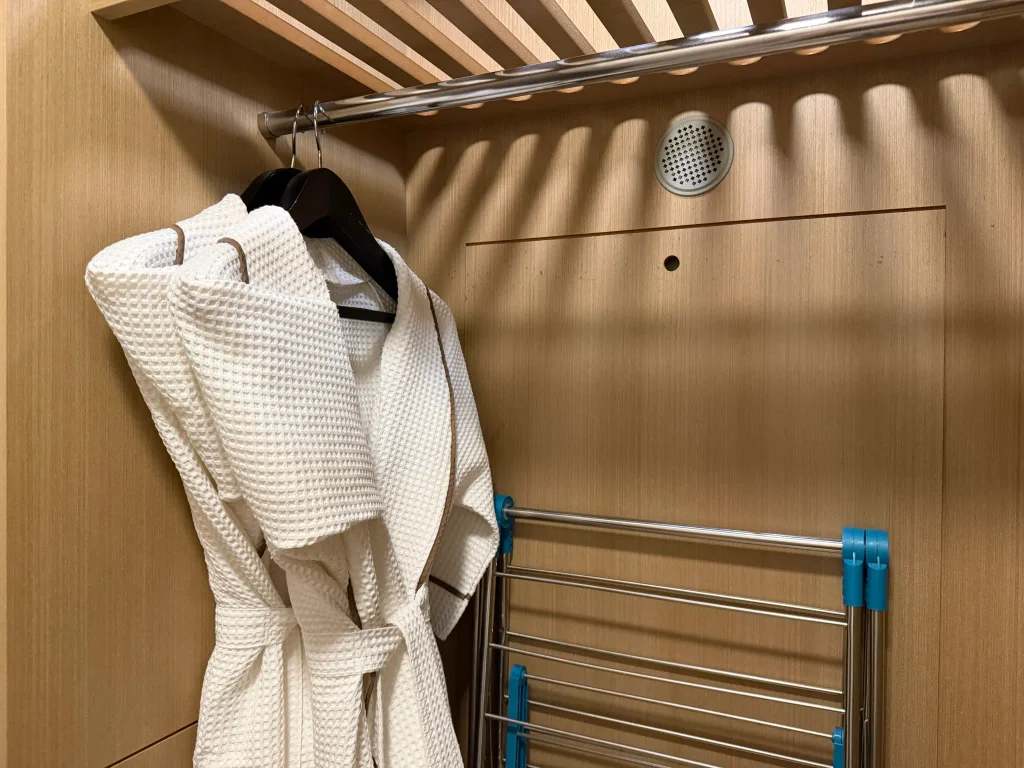 客室のクローゼットに掛けられた白いバスローブと折りたたみ式ラック