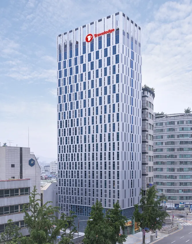 韓国ソウル・東大門のトラベロッジソウル東大門の外観。白い外壁と縦長の窓が特徴的な高層ホテルで、建物上部に赤いTravelodgeのロゴが見える様子。